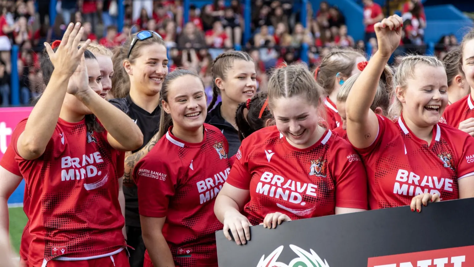 Calum Carpenter Ffion with a group of her team mates on a rugby pitch celebrating their win. They wear red kit and are all smiling. 