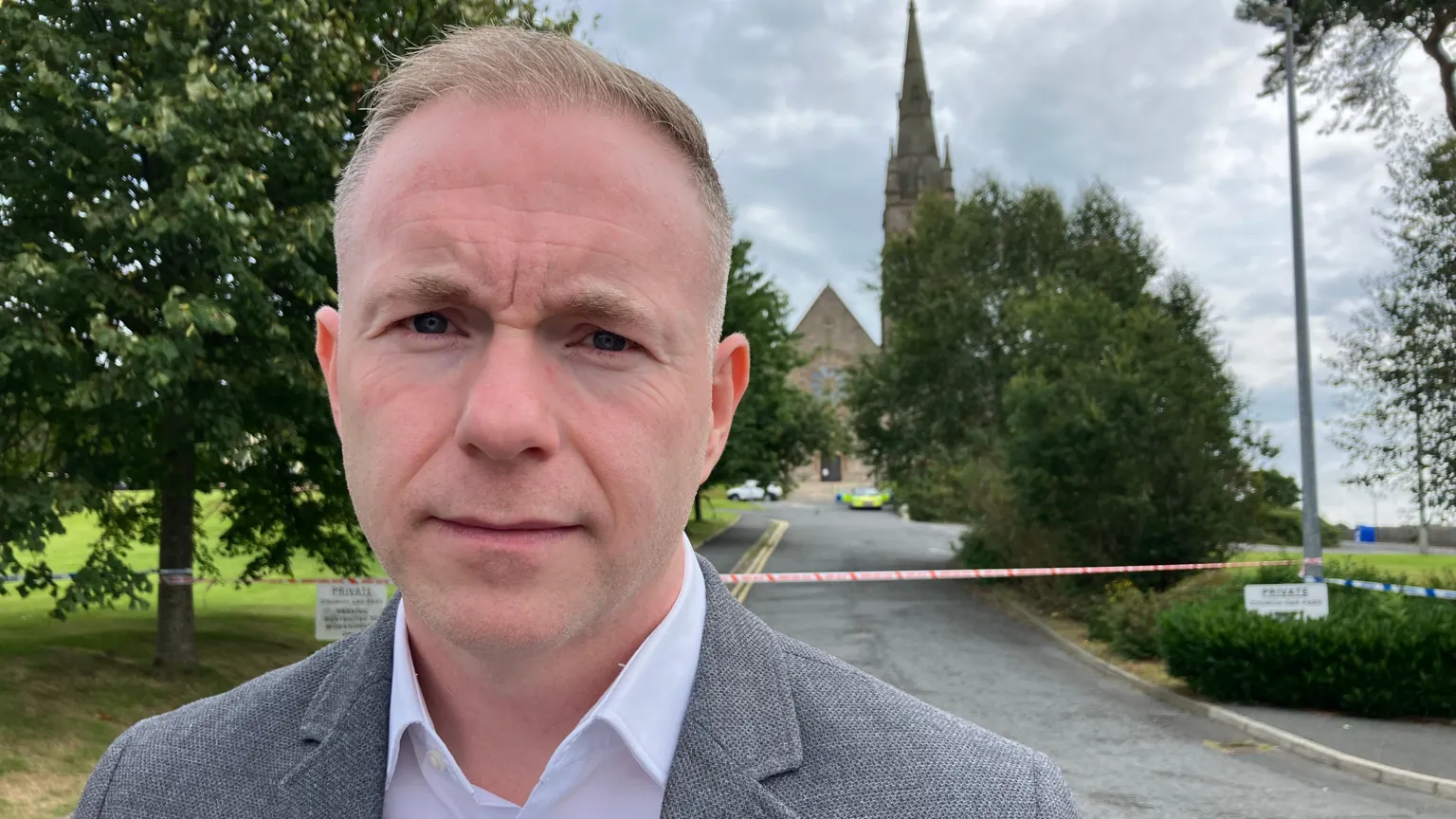 Sinn Féin MP Chris Hazzard, with short grey hair, wearing a white shirt and grey suit.