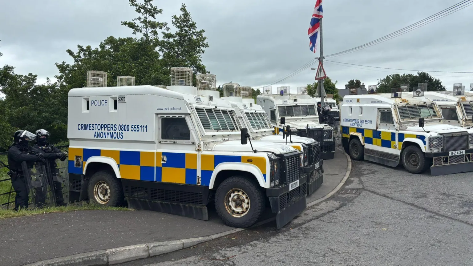 A row of PSNI vans parked on the side of a road.