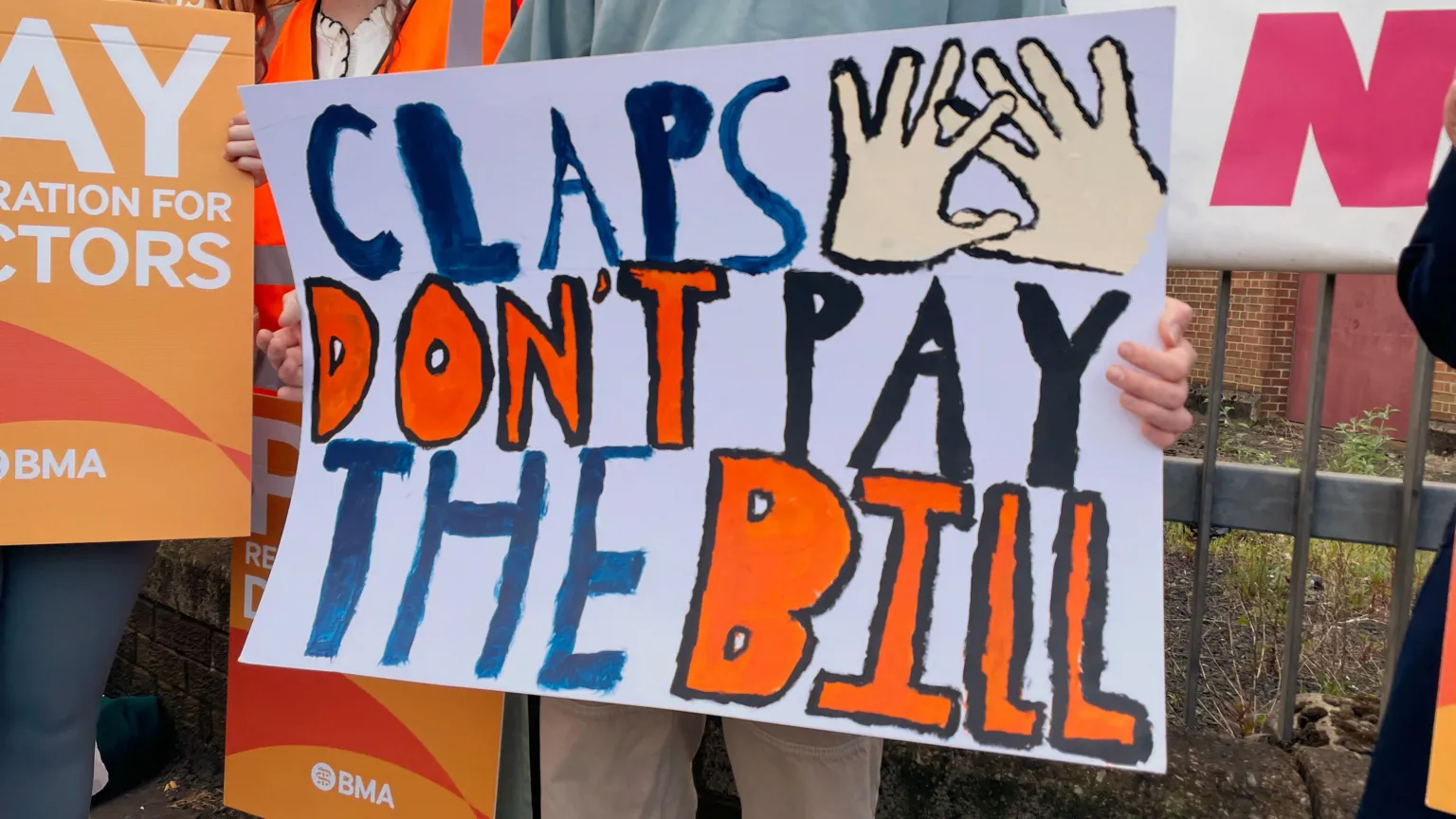 A group of people striking, one has a banner that says claps don't pat the bill.