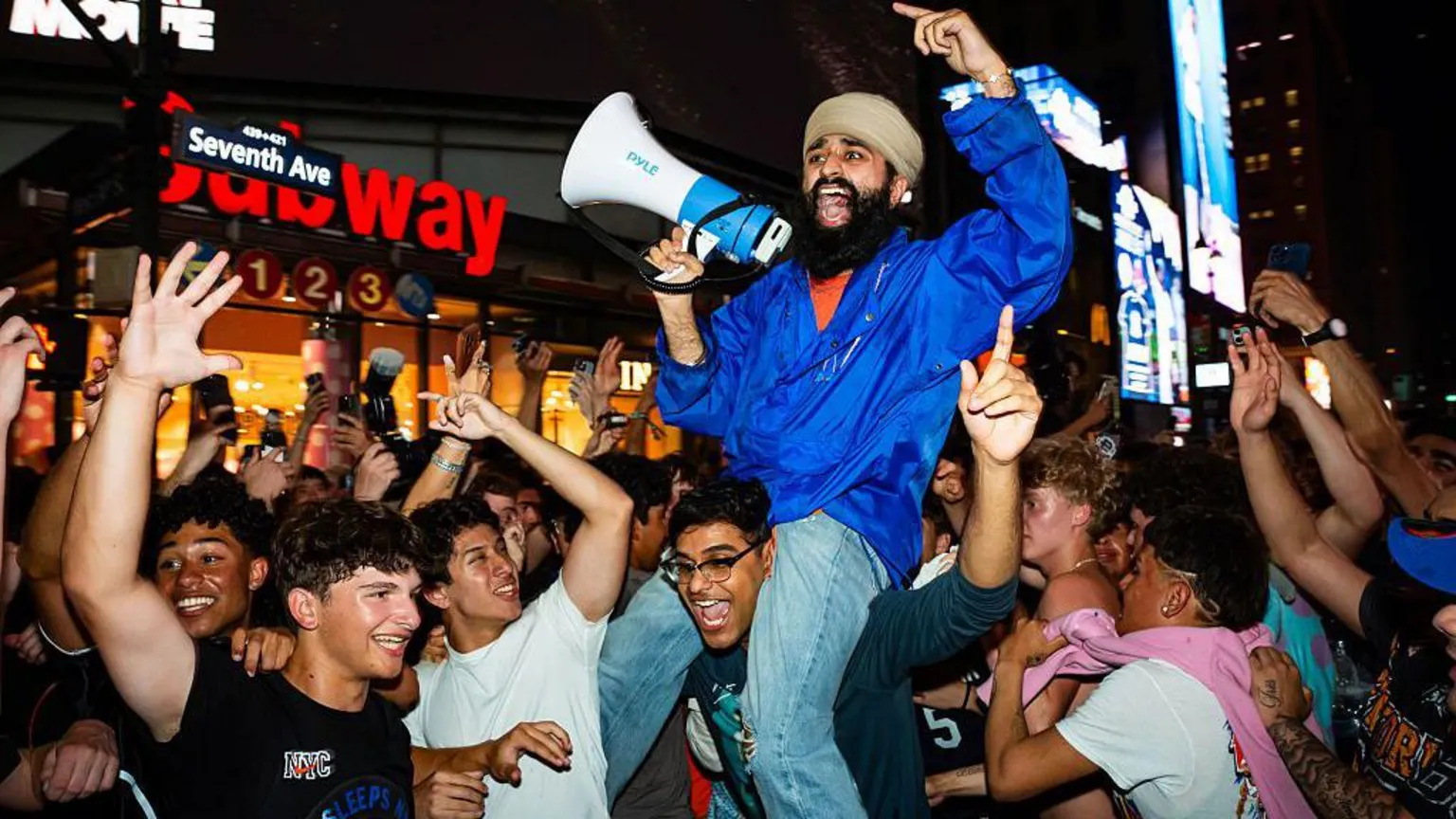 Crowds of fans cheering and celebrating, with one fan sitting on another's shoulders and yelling into a megaphone