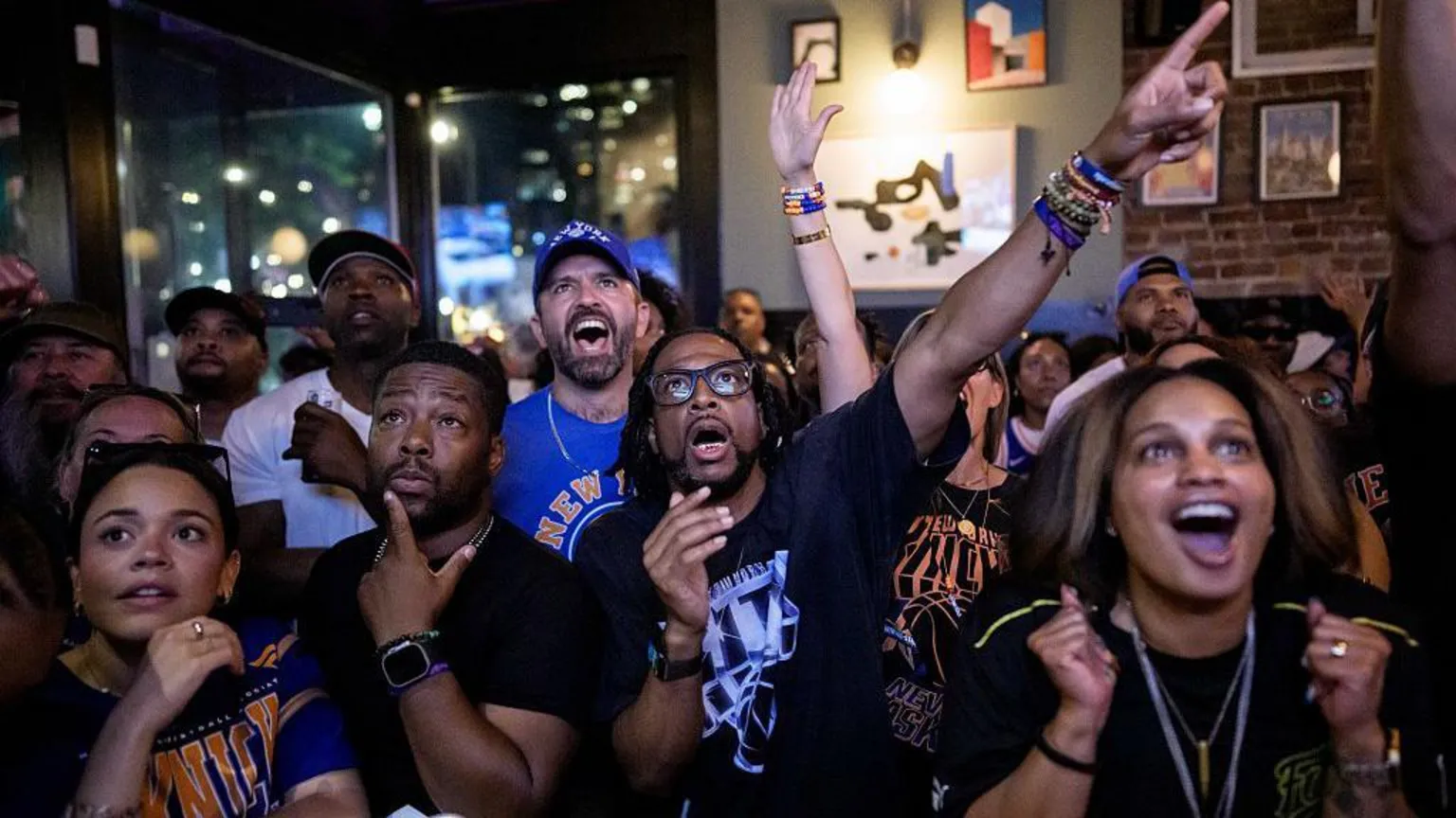 A group of cheering fans wearing Knicks gear in a bar