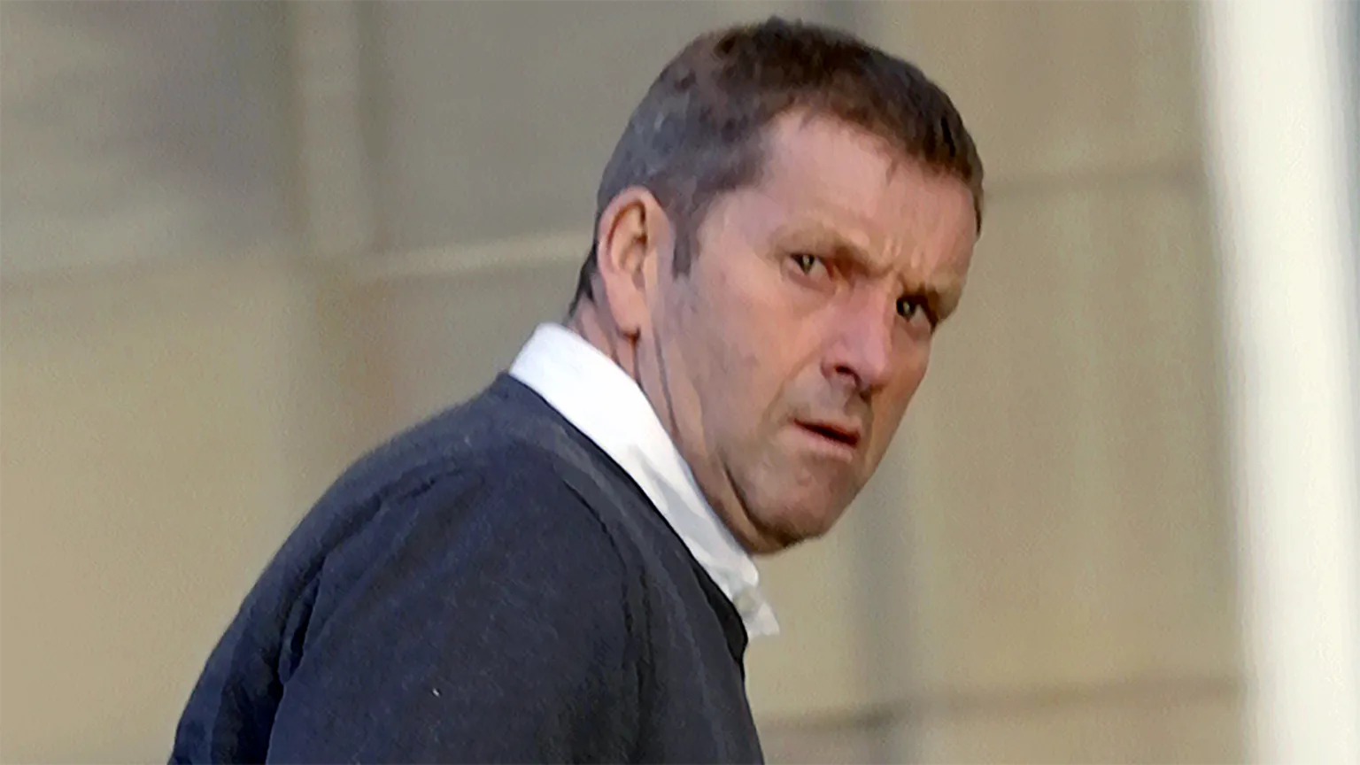 Close-up of Thomas Nicholson in a dark sweater. He is turning his head to look over his shoulder, with a blurred outdoor background