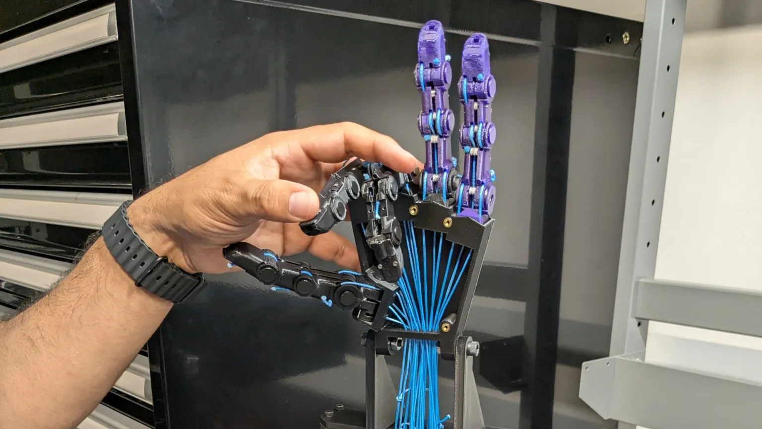Zoe Corbyn A human hand manipulates a robot hand which is on a bench.