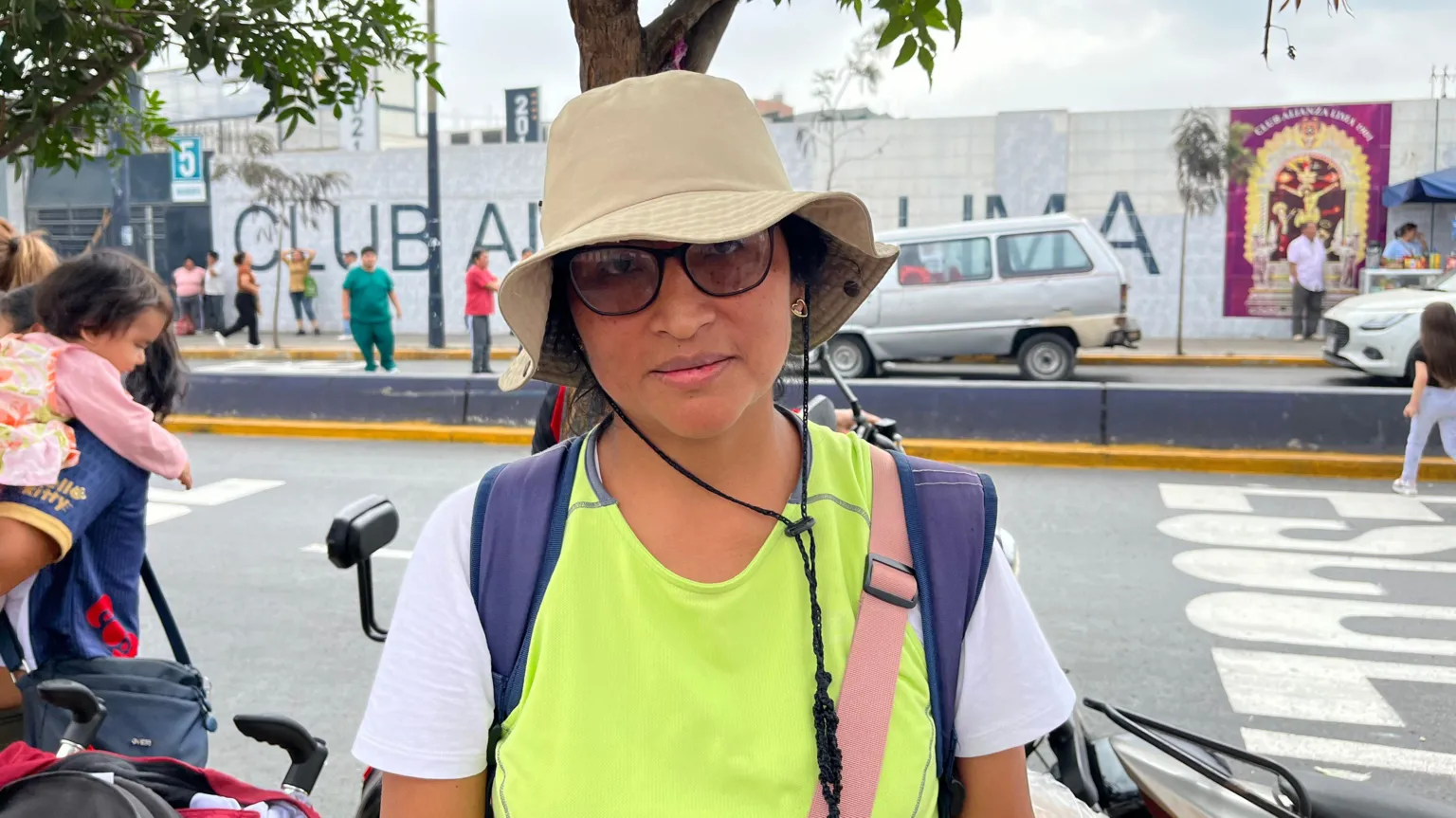 Hilda wears a yellow and white shirt and hat, with glasses and a neutral expression