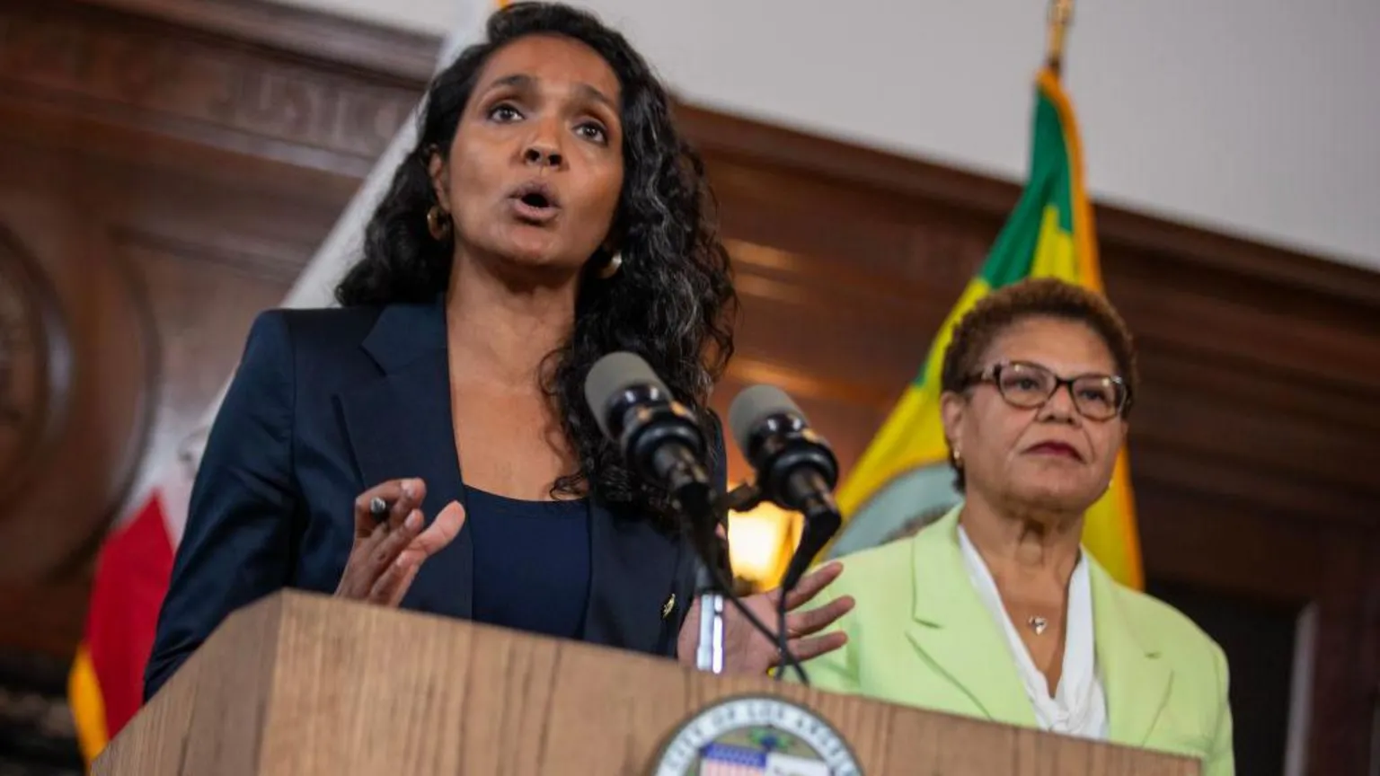 Los Angeles Times via Nithya Raman stands at a podium and microphone with Karen Bass standing alongside her 