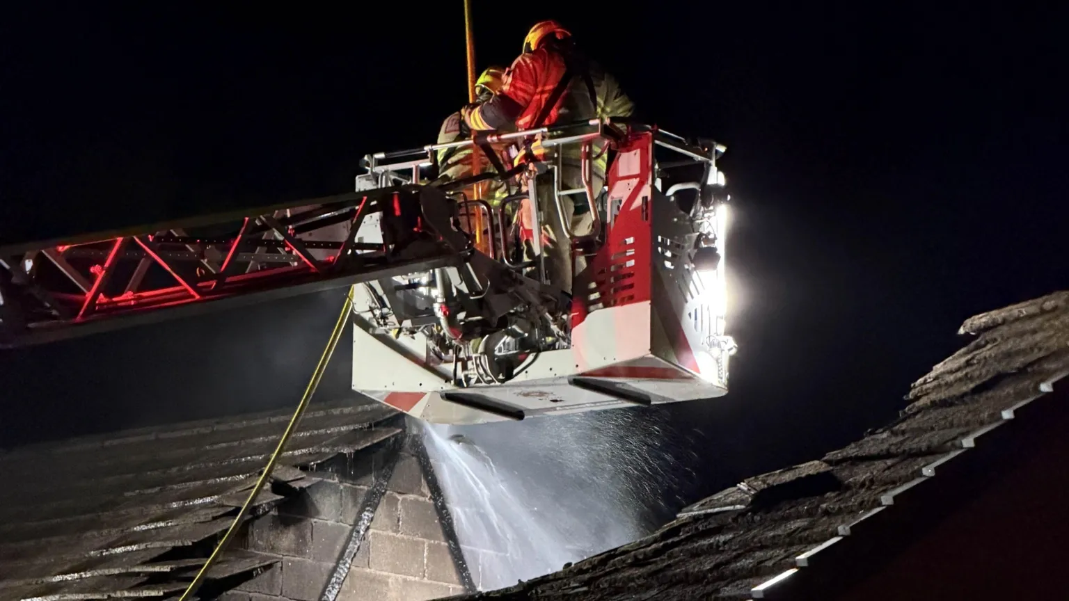 Mid and West Wales Fire Service Two fire fighters seen pouring water into a hole in the roof of a house from a crane
