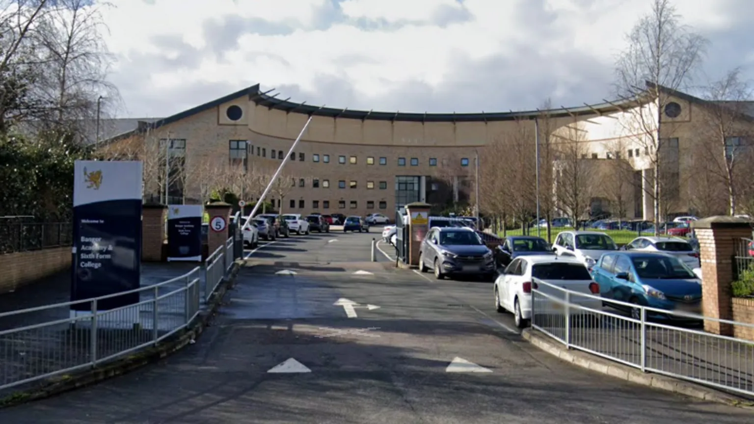 Google Maps The front of Bangor Academy. There is a large brick building, slanted at each side. There is a car park in front of it.
