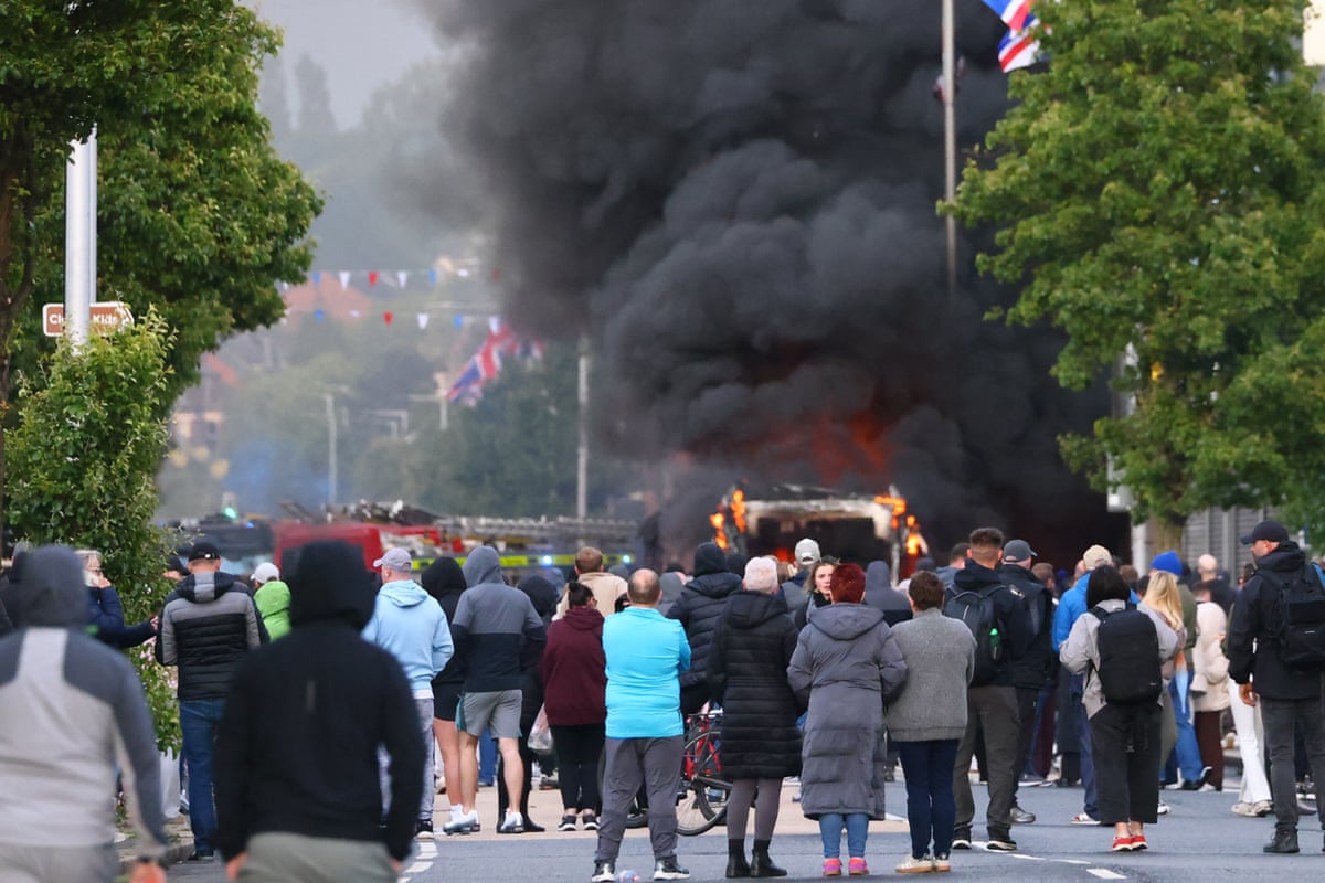 People watch as a vehicle burns during a protest following a stabbing incident in North Belfast.