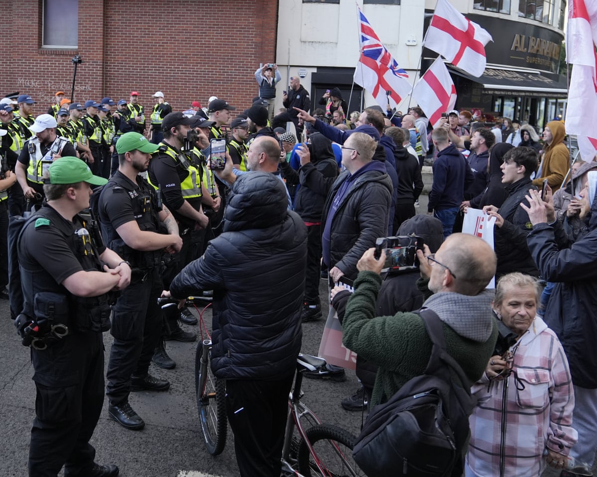 Demonstrators waving UK and England flags angrily confront a line of police officers.