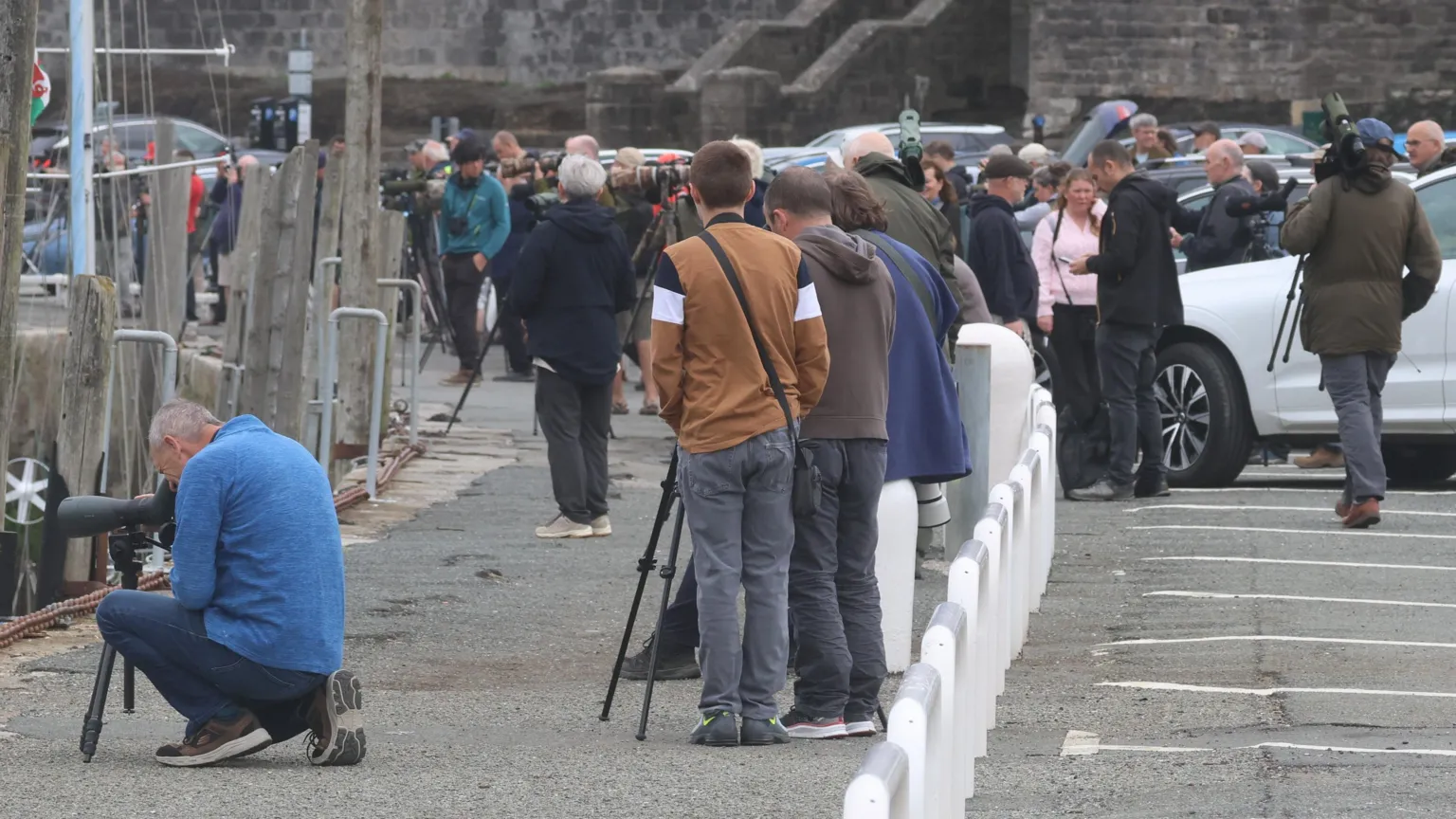 Steve Culley Crowds with cameras gather in a carpark in Caernarfon harbour.