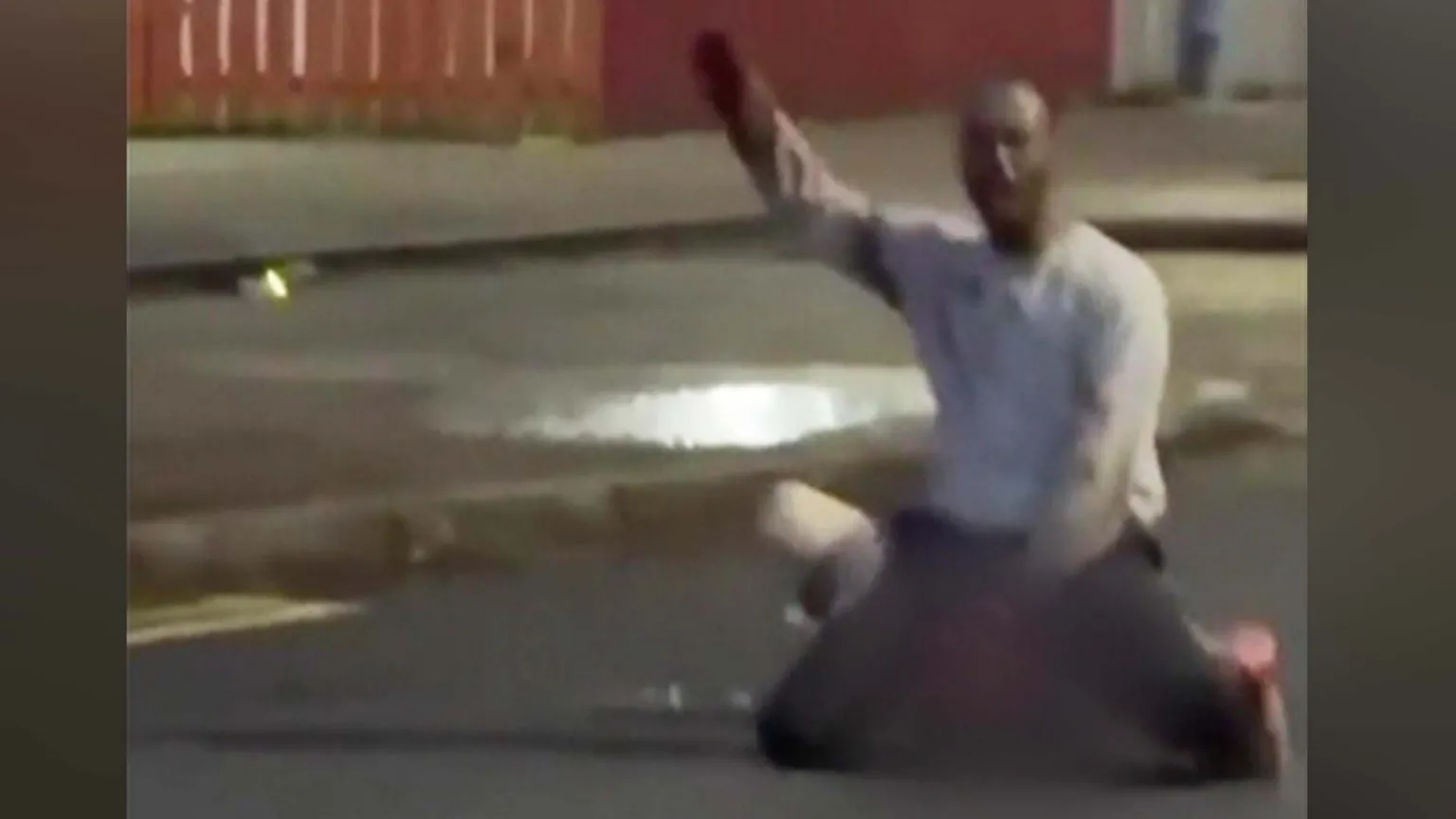 Social Media A image of a man with his hand up in the air while kneeling on the ground over another man, whose face has been blurred