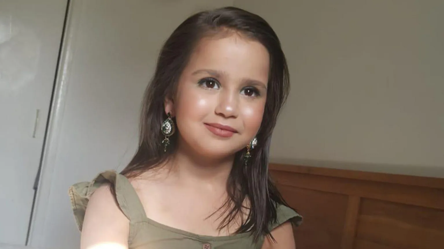 Surrey Police/ Sara Sharif staring off camera dressed in a light coloured dress and wearing earrings