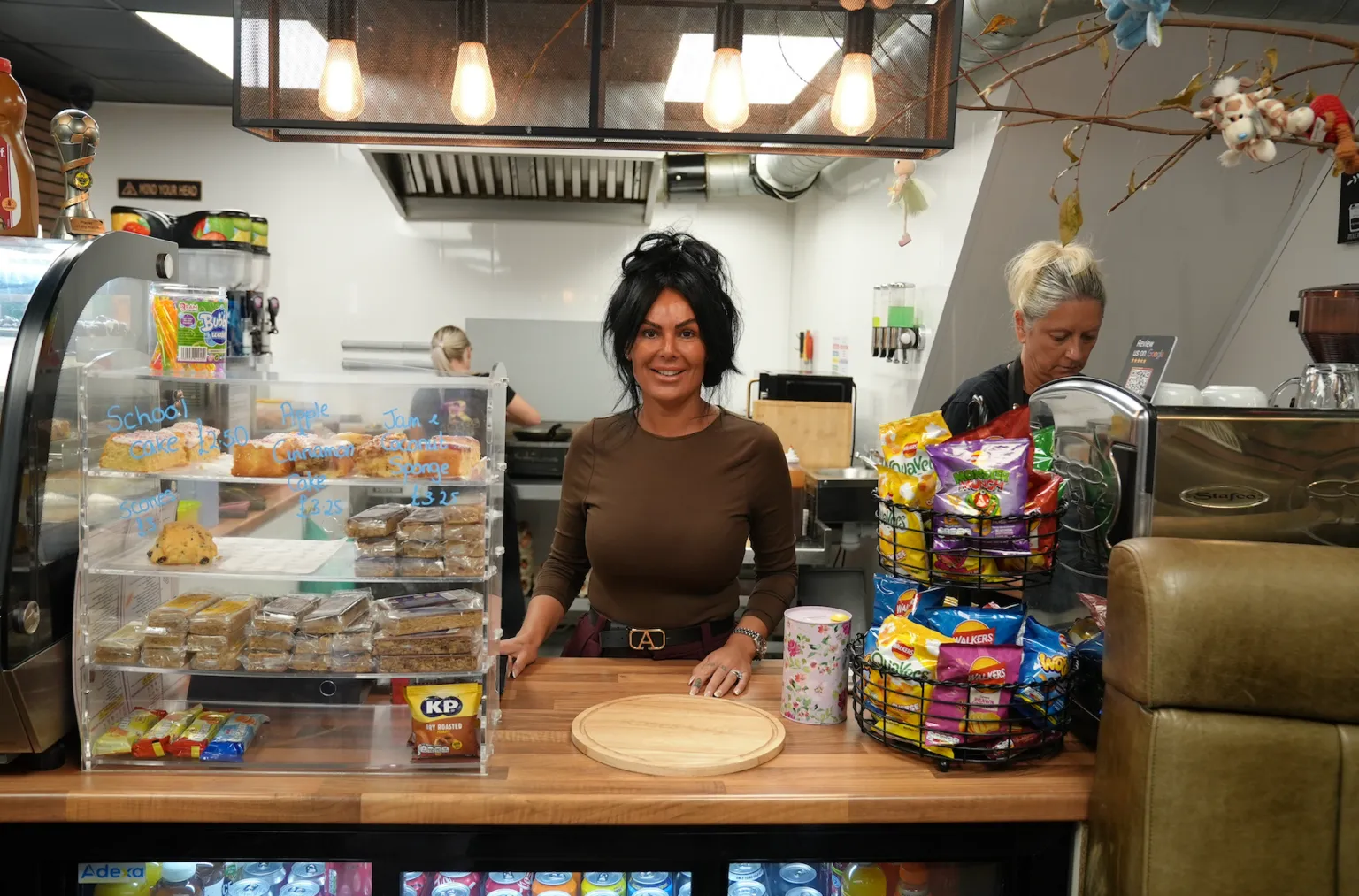 A woman smiles as she stands behind a cafe counter.