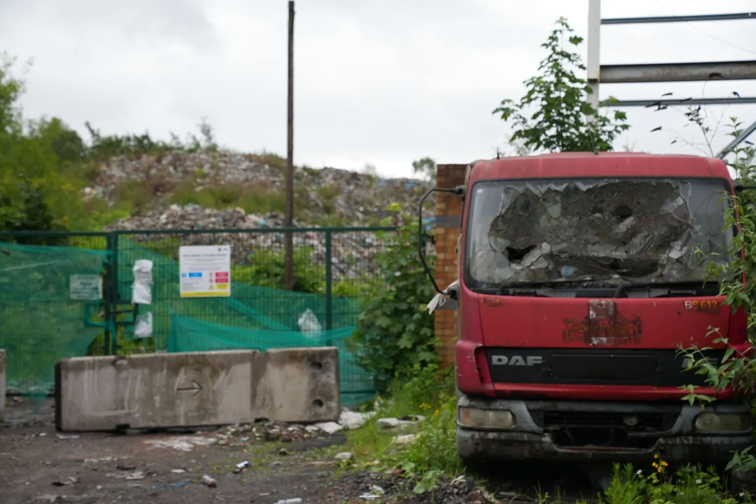 A red truck next to a large waste dump with fencing in front.