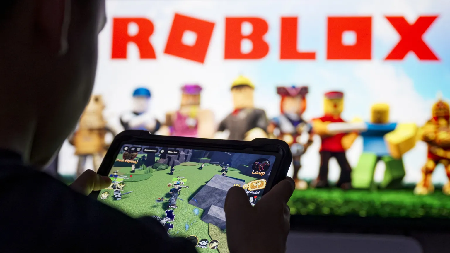 AFP via A young person plays Roblox in front of a larger screen showing the Roblox logo.