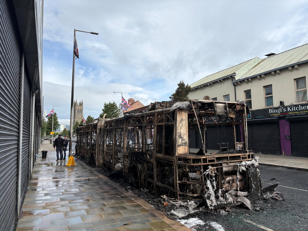 The skeleton of burned bus parked beside a row of shops