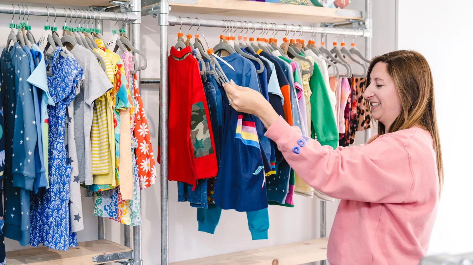 Second Snuggle Ruby Blaken looks at a rack of children's clothes. She has long brown hair and is wearing a pink sweatshirt.