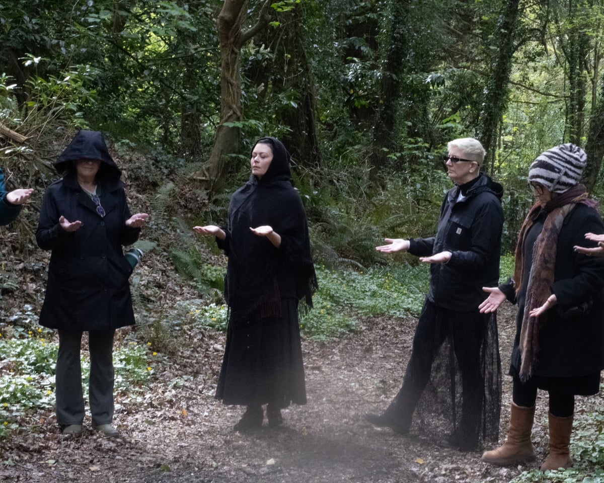 People in black robes stand with their palms up in the forest.