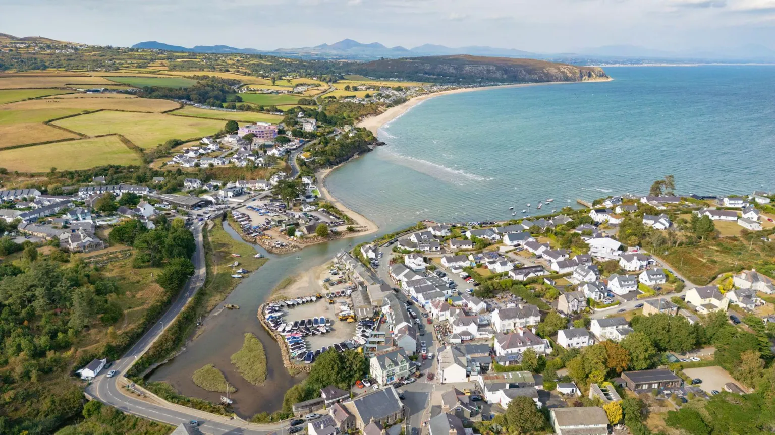 Houses and the sea at Abersoch basked in sunshine. The sea is a clear bright blue and there are grassy fields in the background