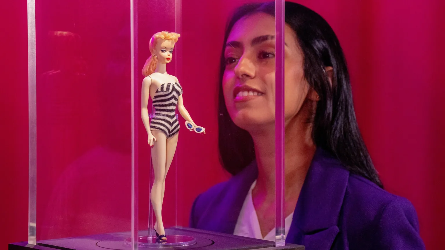 Fatima Zahra Zeyani looks at the very first Barbie doll from 1959 on display during a preview of Barbie: The Exhibition at Kelvingrove Art Gallery and Museum in Glasgow. The figure is in a glass case.