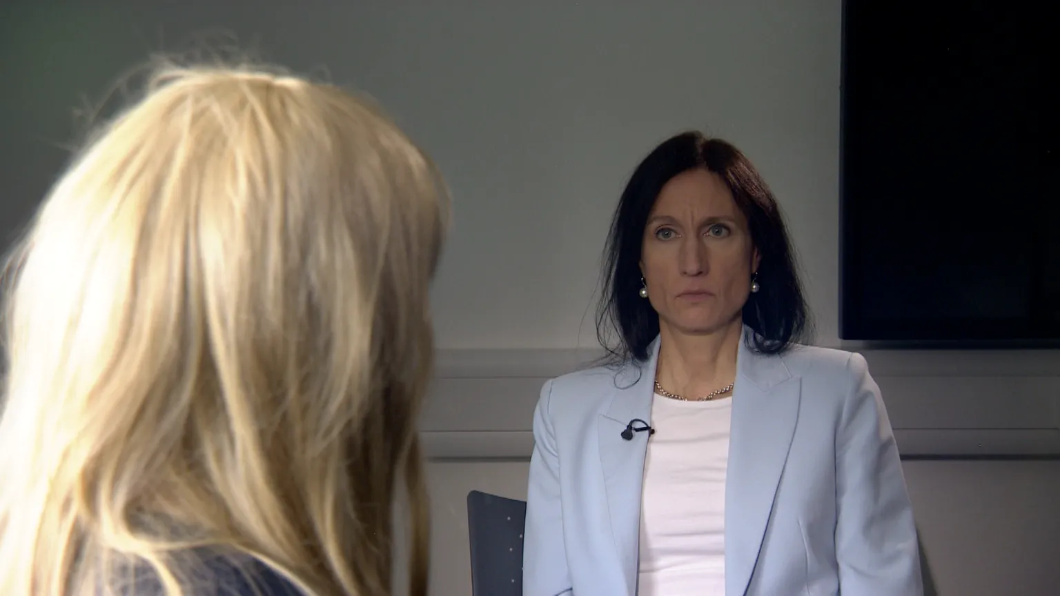 Rear of Joanne's head, showing long blonde hair. She is being interviewed by the BBC's Fiona Trott who is opposite. She has dark brown hair and is wearing a white T-shirt and pale blue jacket.
