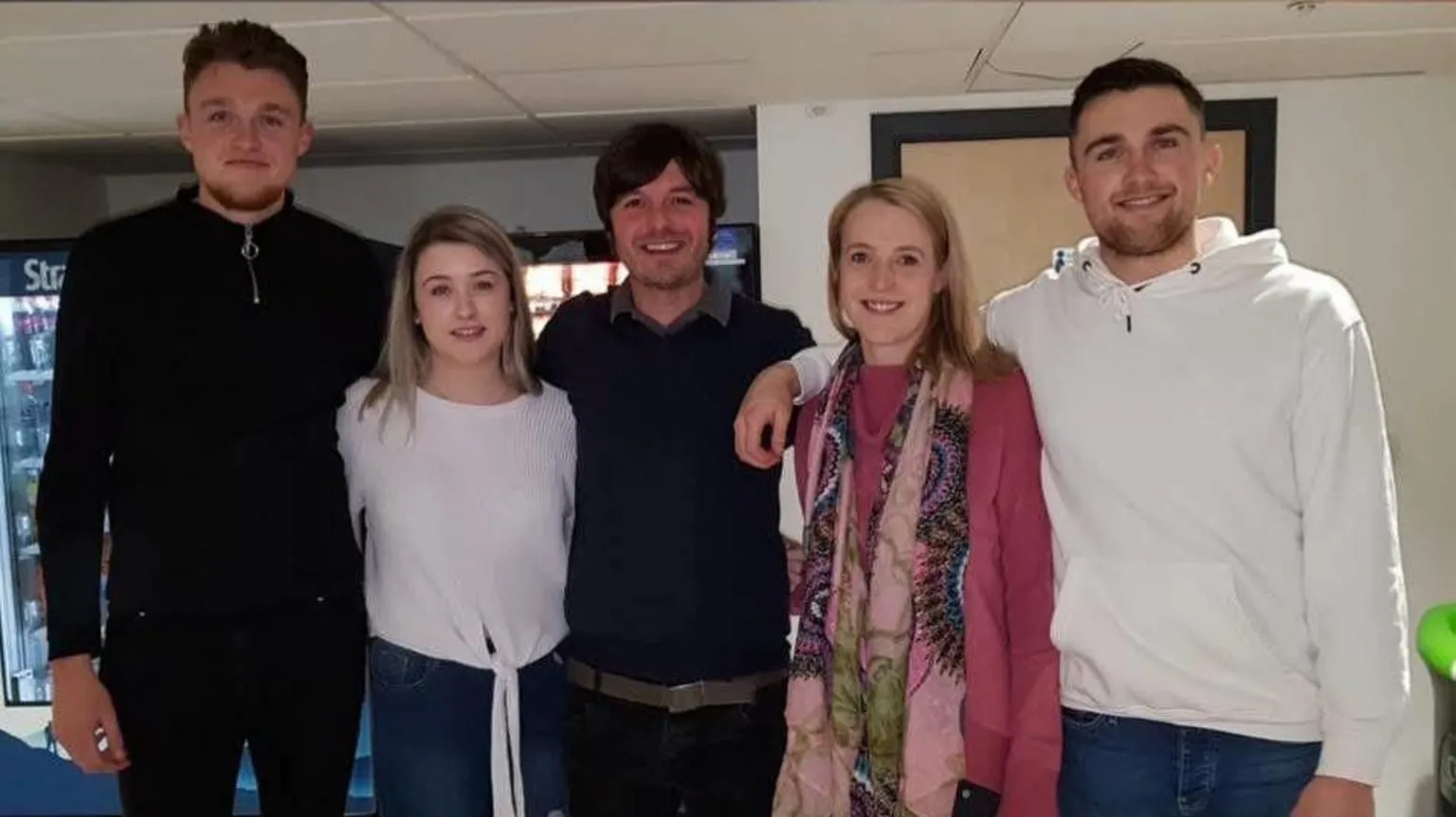 Souttar family Five young people in casual dress standing in a row in what appears to be an office. They have their arms around one another and are smiling. There are three men and two women.
