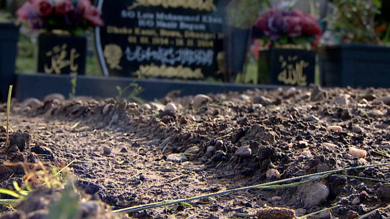 A photo of mud in the ground and in the background you can see a gravestone. 