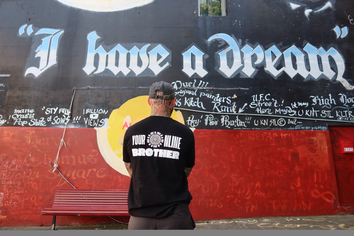 A man wearing a shirt that says “Your online brother” is seen from behind looking at a mural featuring the Aboriginal flag colours and the words “I have a dream”