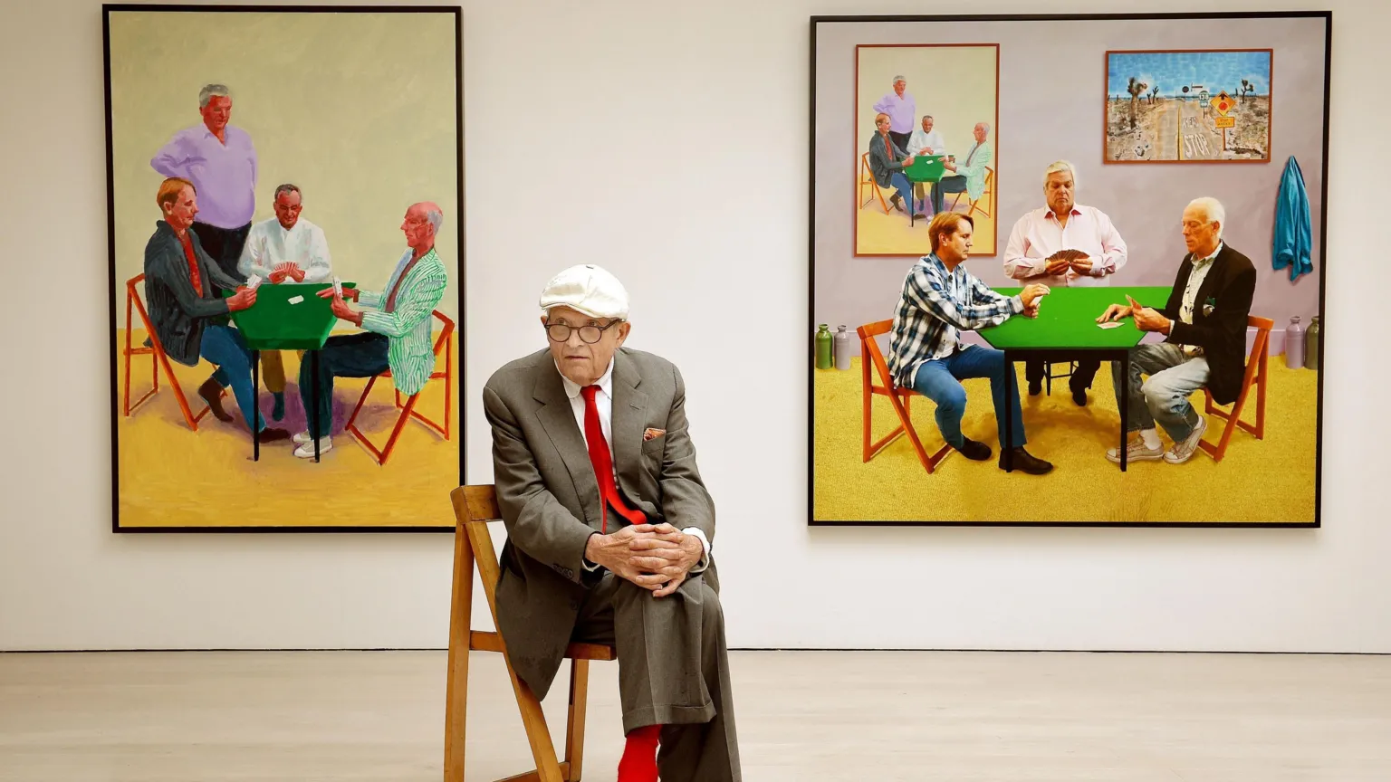David Hockney sits in a brown suit with a red tie. He's in front of his work entitled Card Players (left) and A Bigger Card Players at the launch of an Exhibition of his work called David Hockney: Painting And Photography at Annely Juda Fine Art in central London.