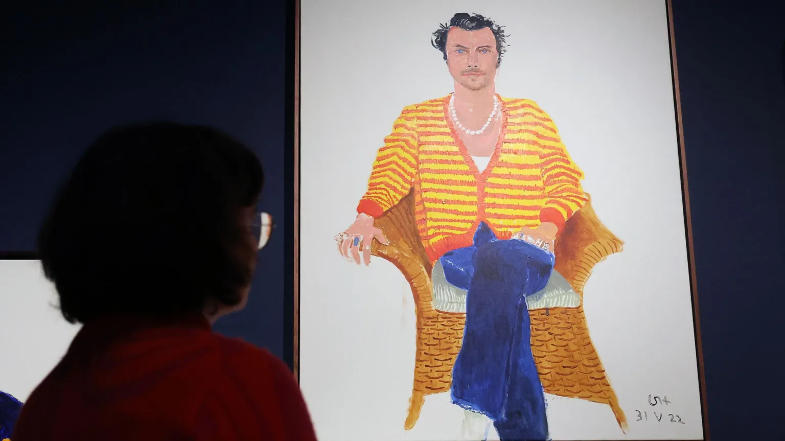 EPA A person looks at a painting of Harry Styles, who sits in a red and yellow striped jumper and blue jeans