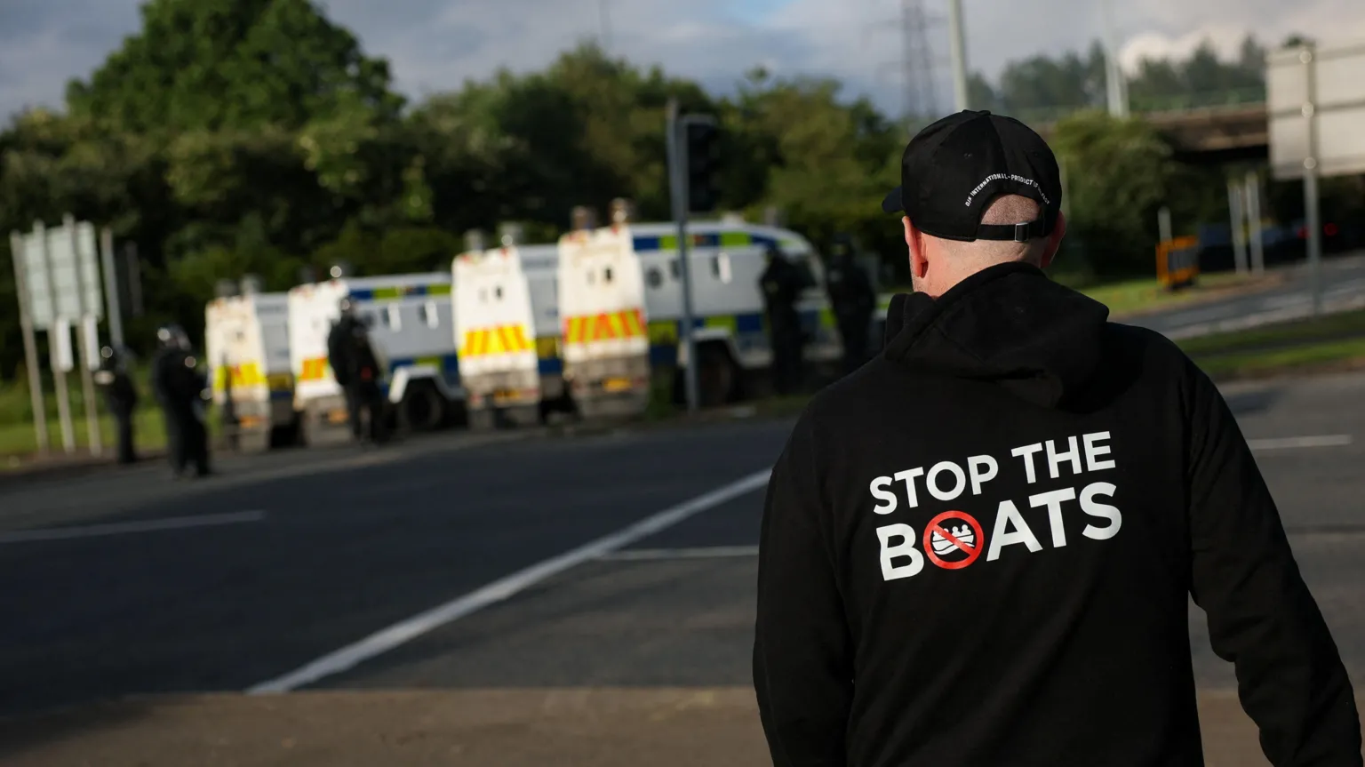 A man wears a 'Stop the Boats' hoody, as police and their vehicles block a road to stop anti-immigrant protesters from reaching Sandyknowes Roundabout.