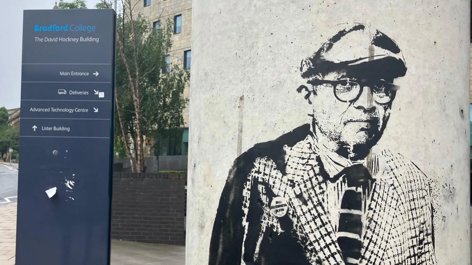 BBC/Grace Wood A graffiti image of David Hockney on a pillar. Behind in a sign showing directions around Bradford College