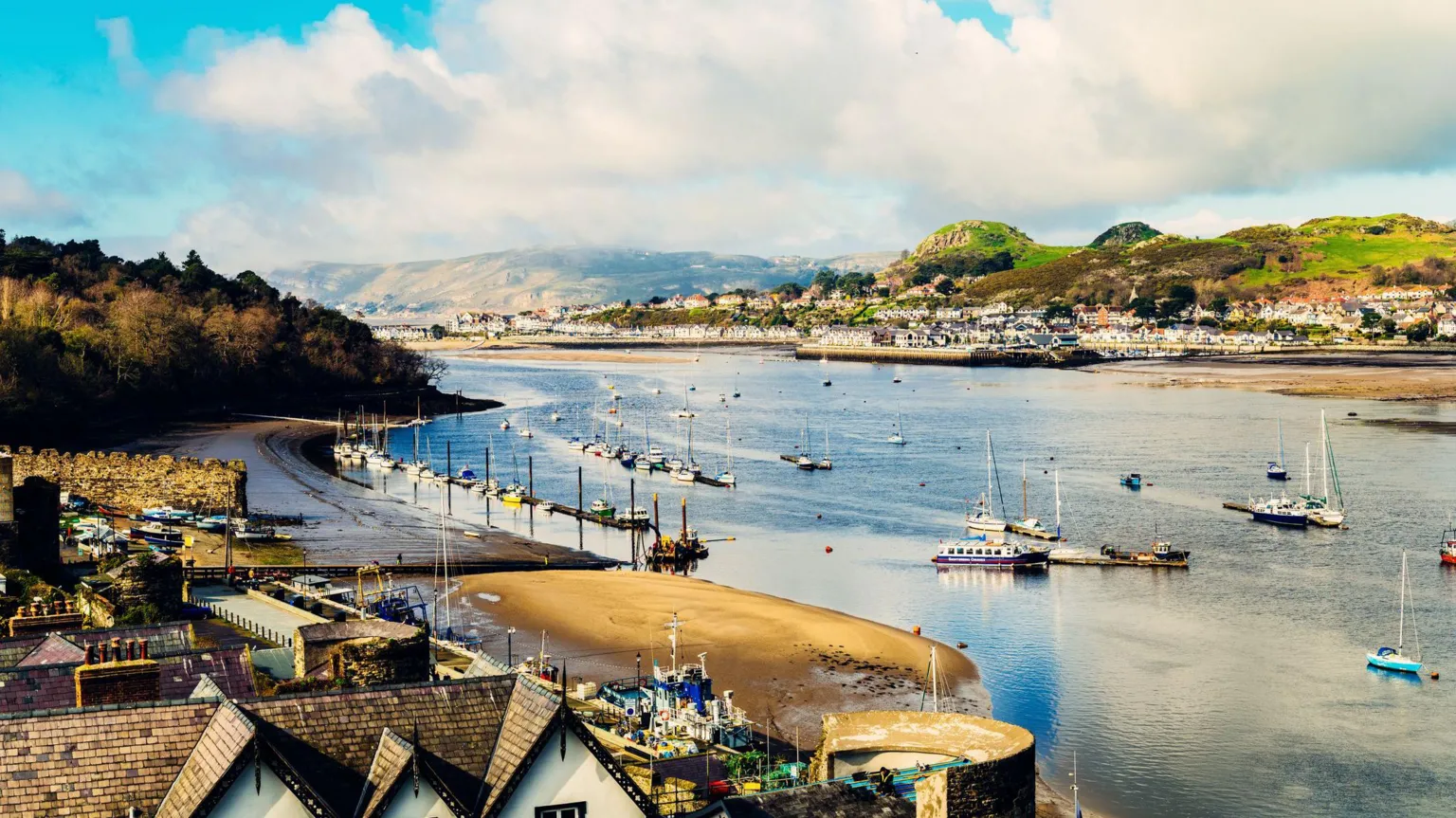 Looking north east from the town of Conwy across the bay. There are a number of sailing boats on the water with hills and houses in the background.