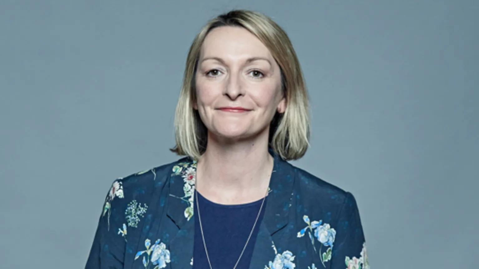 Jess Morden head shot. She has a blonde bob and smiles at the camera. She has a blue top with a silver chain and a blue and flowery blazer on.