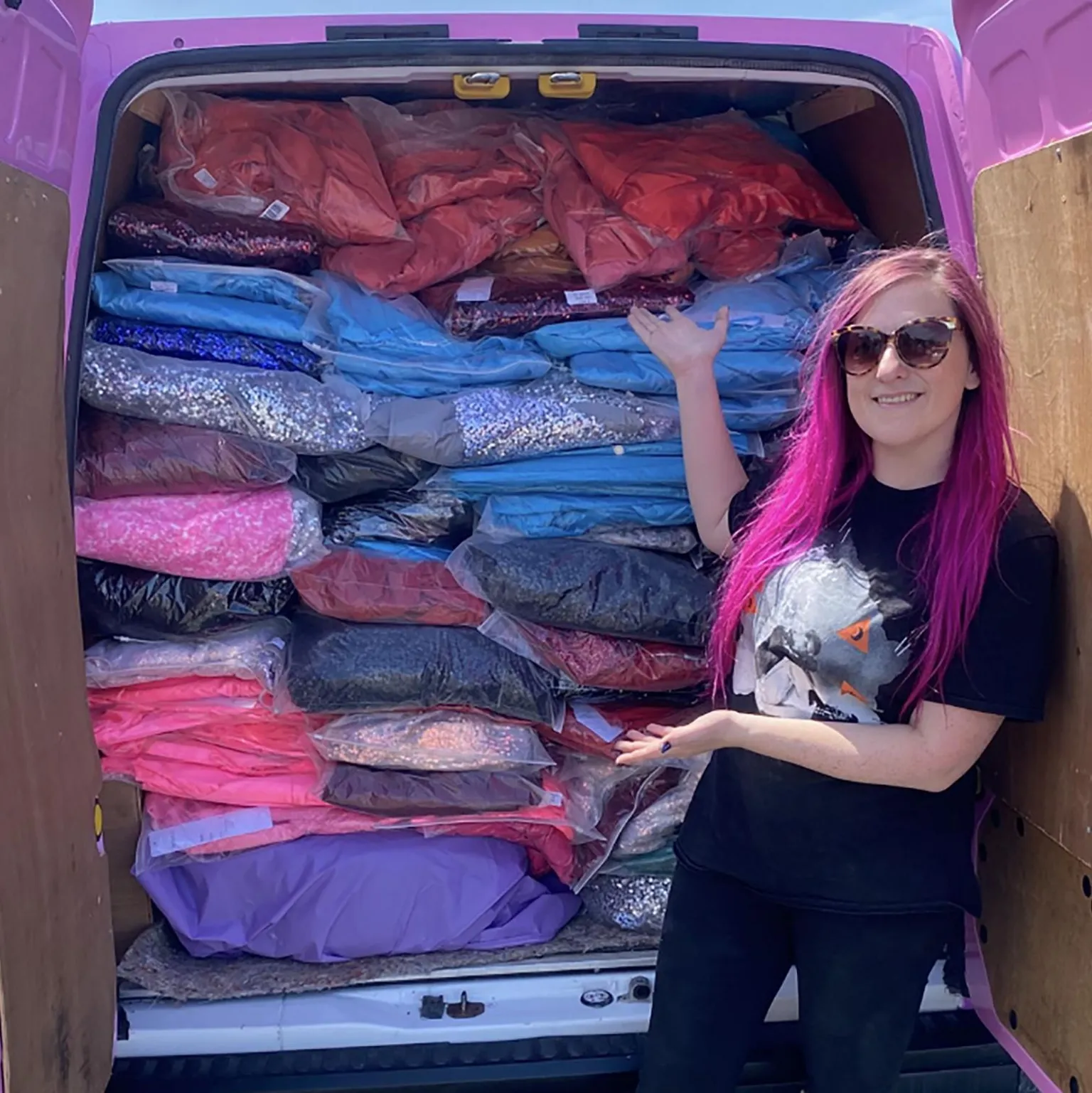 Ally Outten/ A woman with long purple hair showing prom dresses in the back of a van. Ally wears sunglasses and a black t-shirt and jeans.