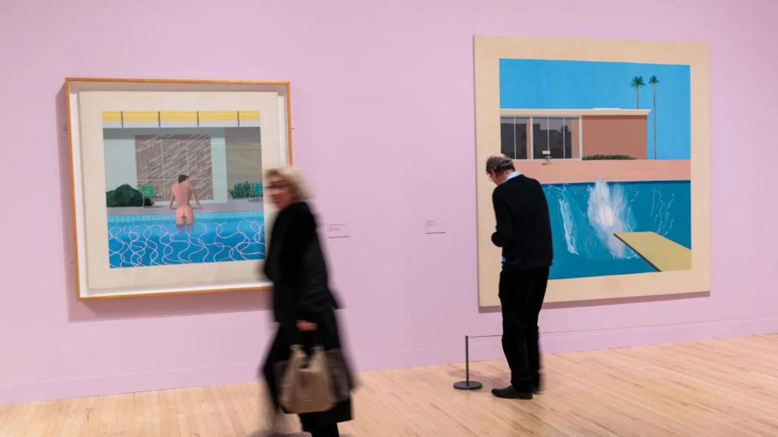 Two museum goers walk past the swimming pool paintings of David Hockney