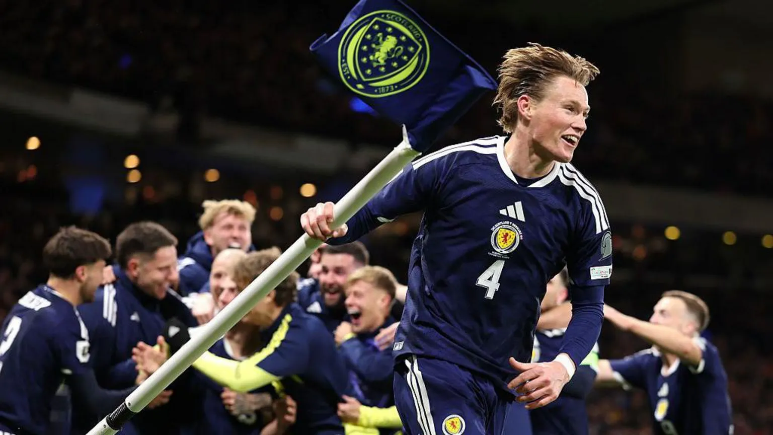 Scotland player Scott McTominay holds up a corner flag as part of a celebration, with his team mates celebrating in the background