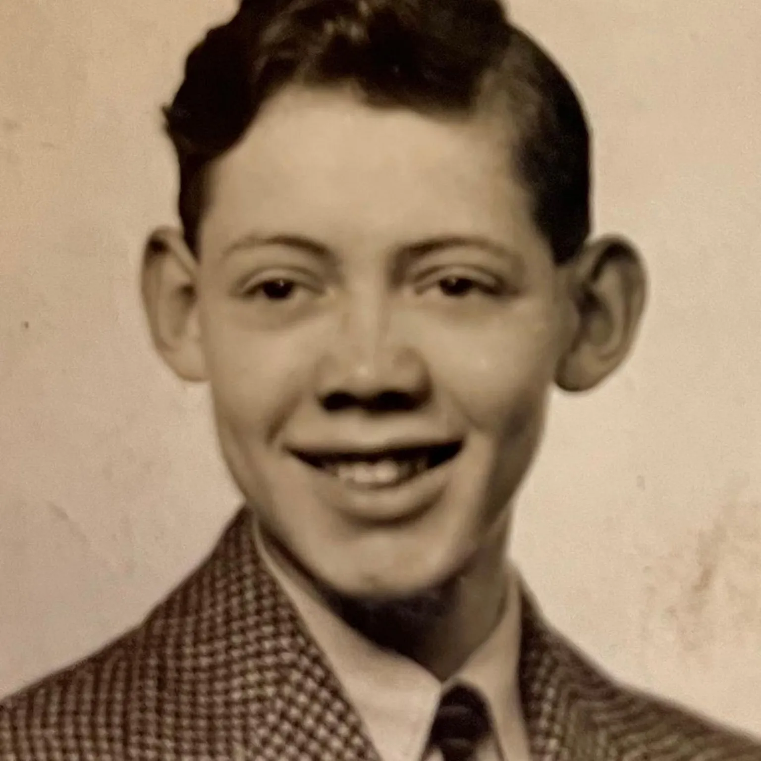 Vintage black-and-white portrait of Iain from around the time he took the 195=47 test. He has short, neatly styled hair, wearing a patterned jacket and tie, looking slightly to the side against a plain studio background.