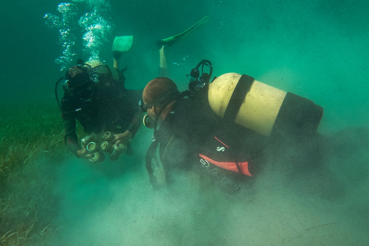 Two scuba divers clean up plastic and tins in murky water, Playa Larga, Cuba.