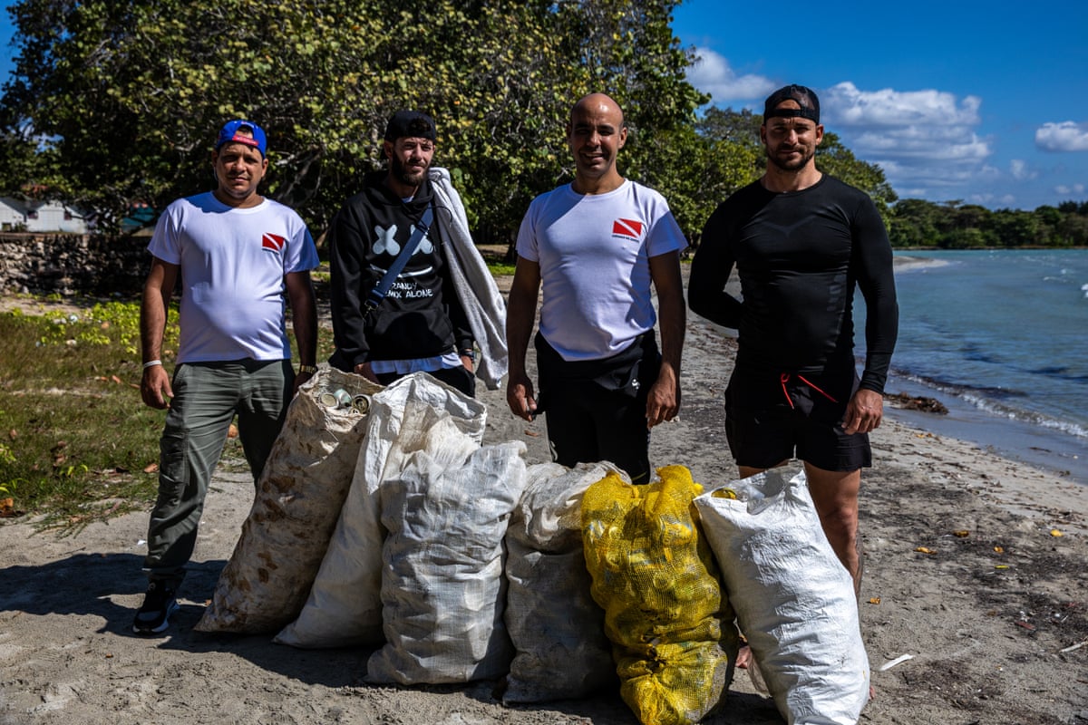 Four men on a beach pose with sacks of plastic rubbish and tins they have collected.