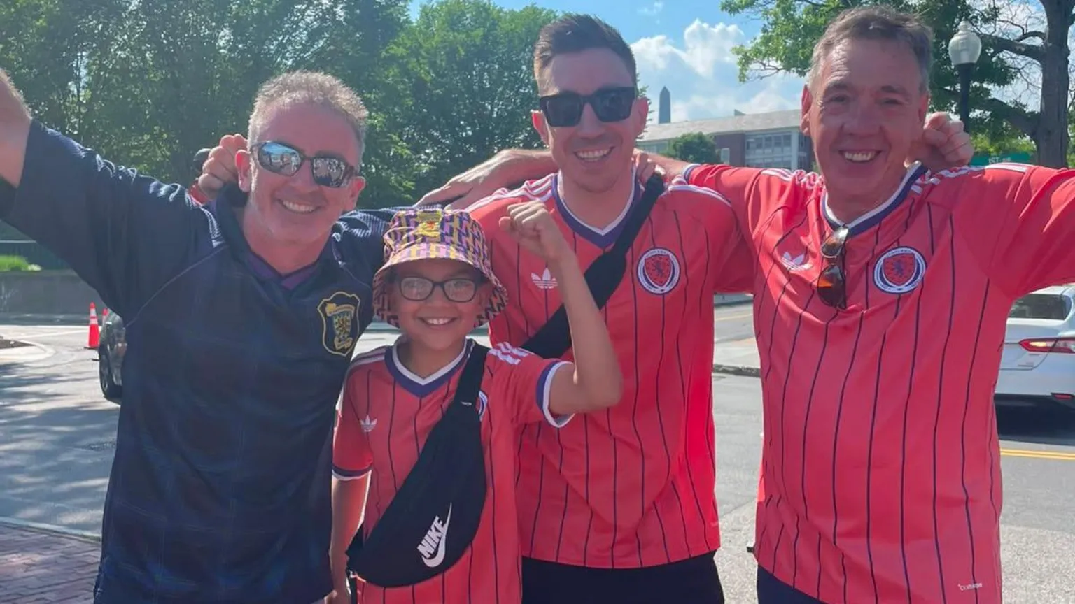 Four men wearing Scotland football tops with their hands in the air