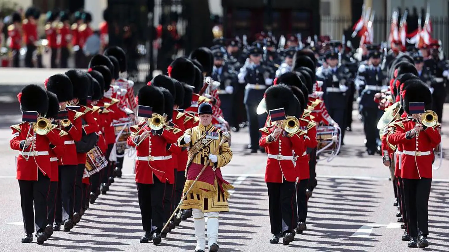 Musicians from the Massed Bands of the Household Division parade during Trooping The Colour on June 13, 2026 in London, England. Four lines of musicians walk wearing a full red, white and black uniform, all of which are playing brass instruments. They are led by a man in the front and centre, wearing a smaller hat and wearing a sash.