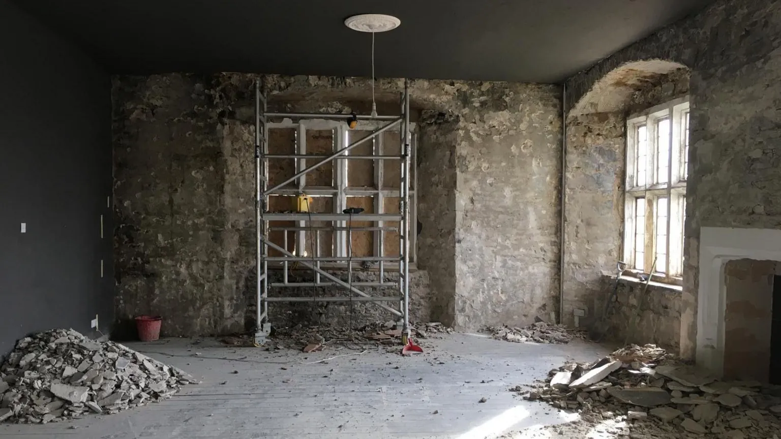 Christine Tallon A stripped back room being renovated. There is piles of plaster on the floor and scaffolding inside the room.