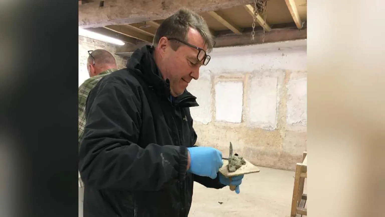 Christine Tallon Adrian Cole putting some cement on a slab. He is wearing a black jacket, blue gloves and has glasses propped on his forehead.