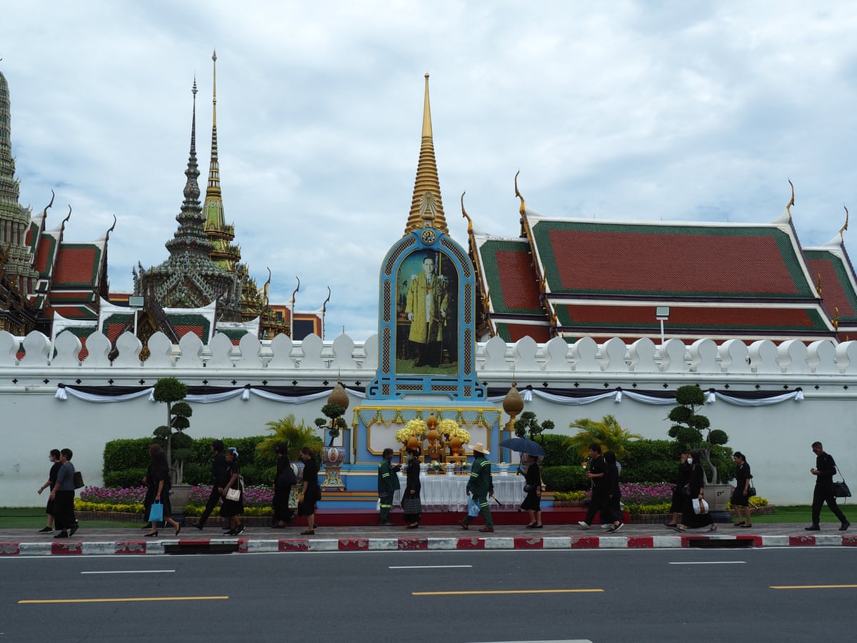 People walk along a pavement outside the Grand Palace