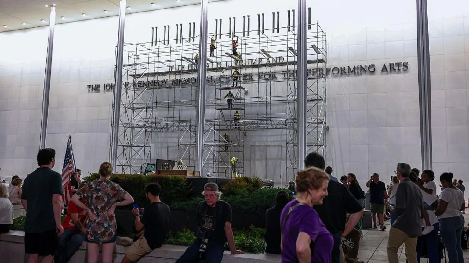 People mill about in front of scaffolding on the front of the Kennedy Center