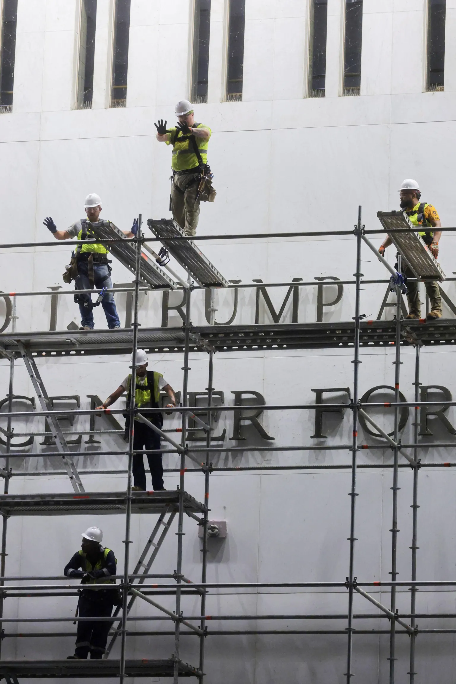 Workers stand on scaffolding in front of the sign and gesture