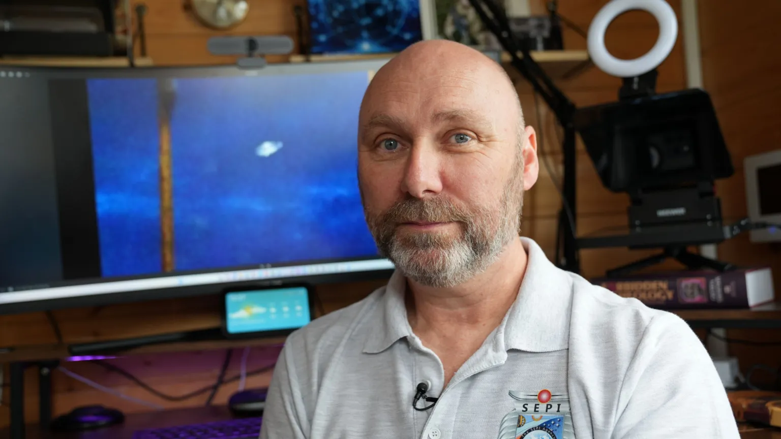 John Fairhall/BBC David Jon is wearing an off-white polo shirt while sitting at a desk. He is looking directly at the camera and has a beard.