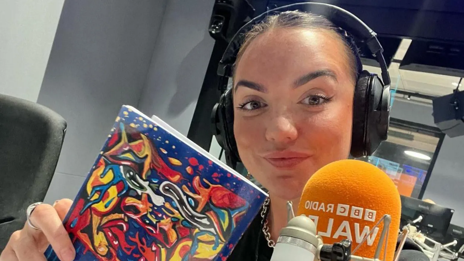 Georgia Griffiths A selfie of Georgia sat in a BBC Radio Wales studio holding her poetry book and wearing blach headphones. She smiles looking at the camera. 
